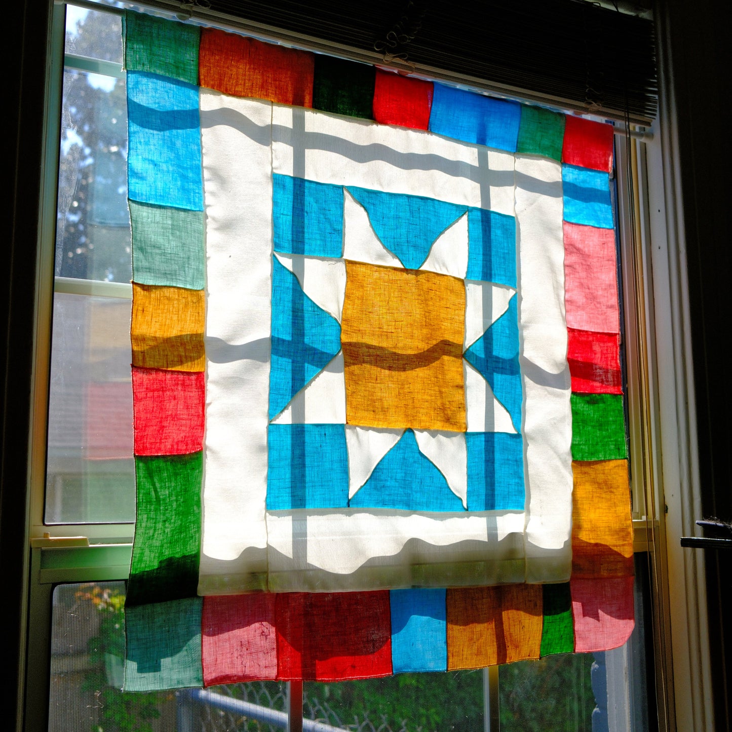 Colorful quilt with geometric pattern hanging on a window in sunlight