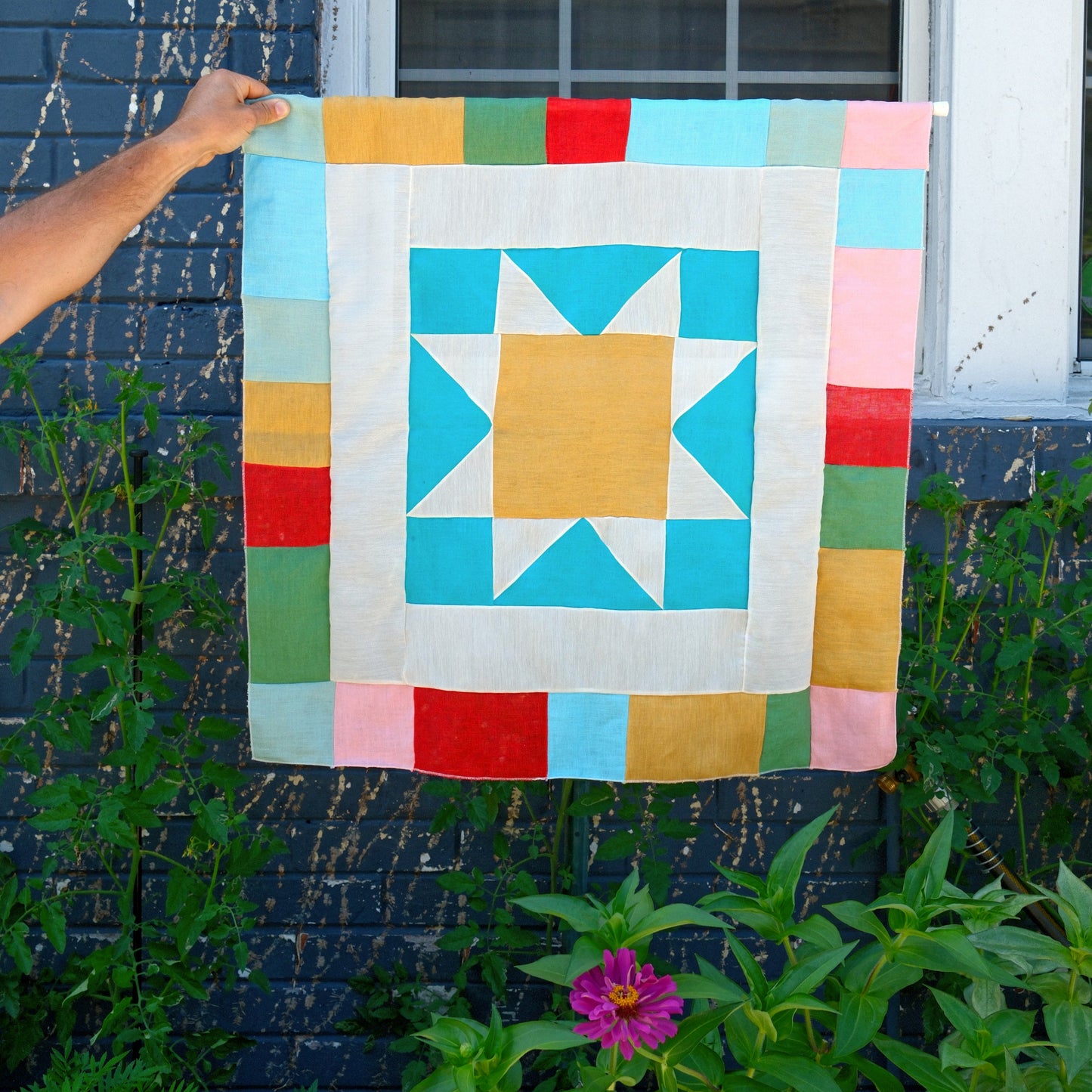 Colorful quilt with star pattern held up against a brick wall.
