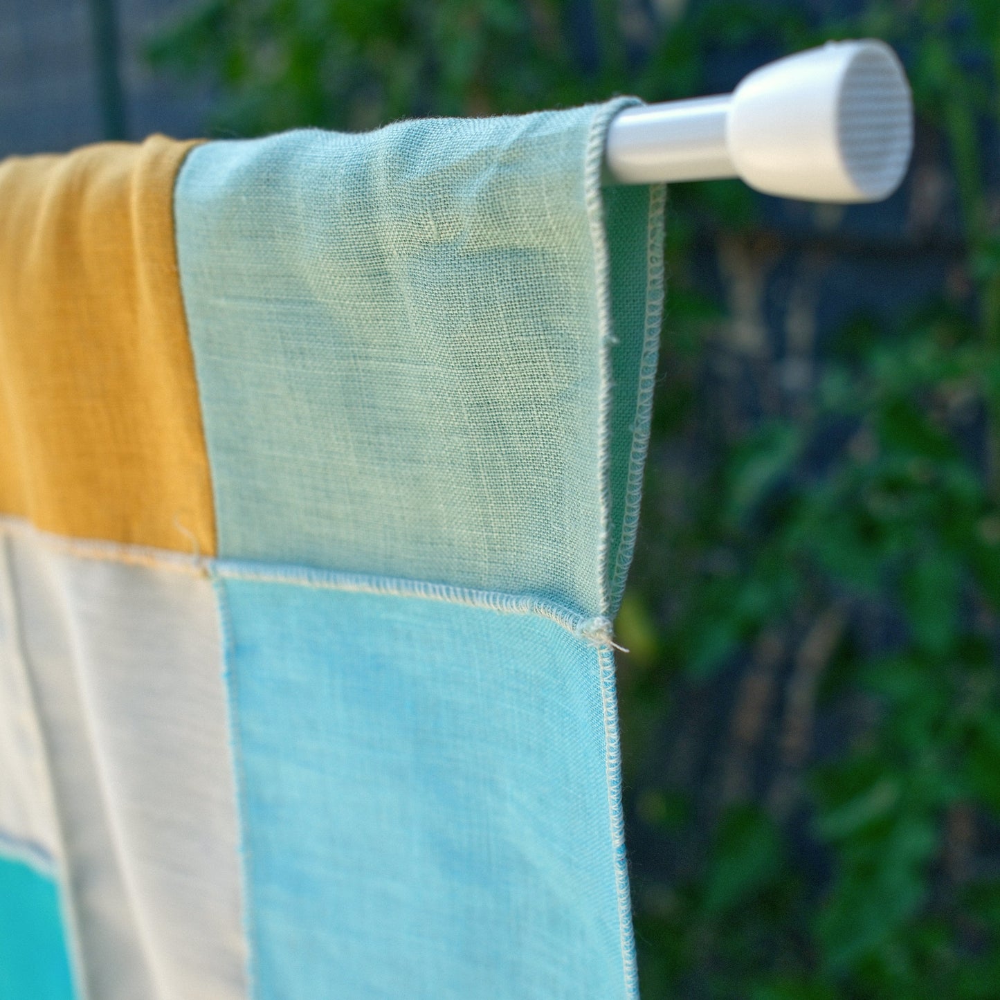 Colorful linen curtain hanging on a white rod with a blurred green background